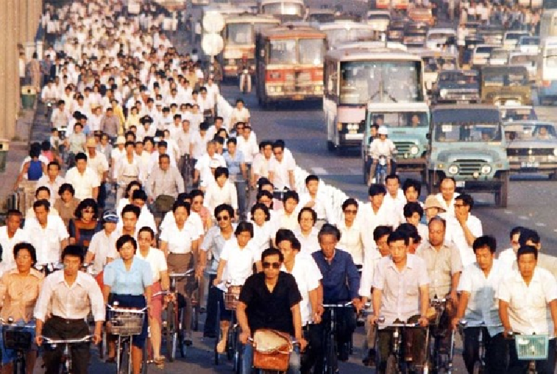 Photo from the 1990's showing white-collar commuters on a busy cycleway. There's exceptionally more cyclists than cars.